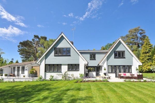 Modern family home exterior showcasing a large lawn and garden under a clear blue sky.